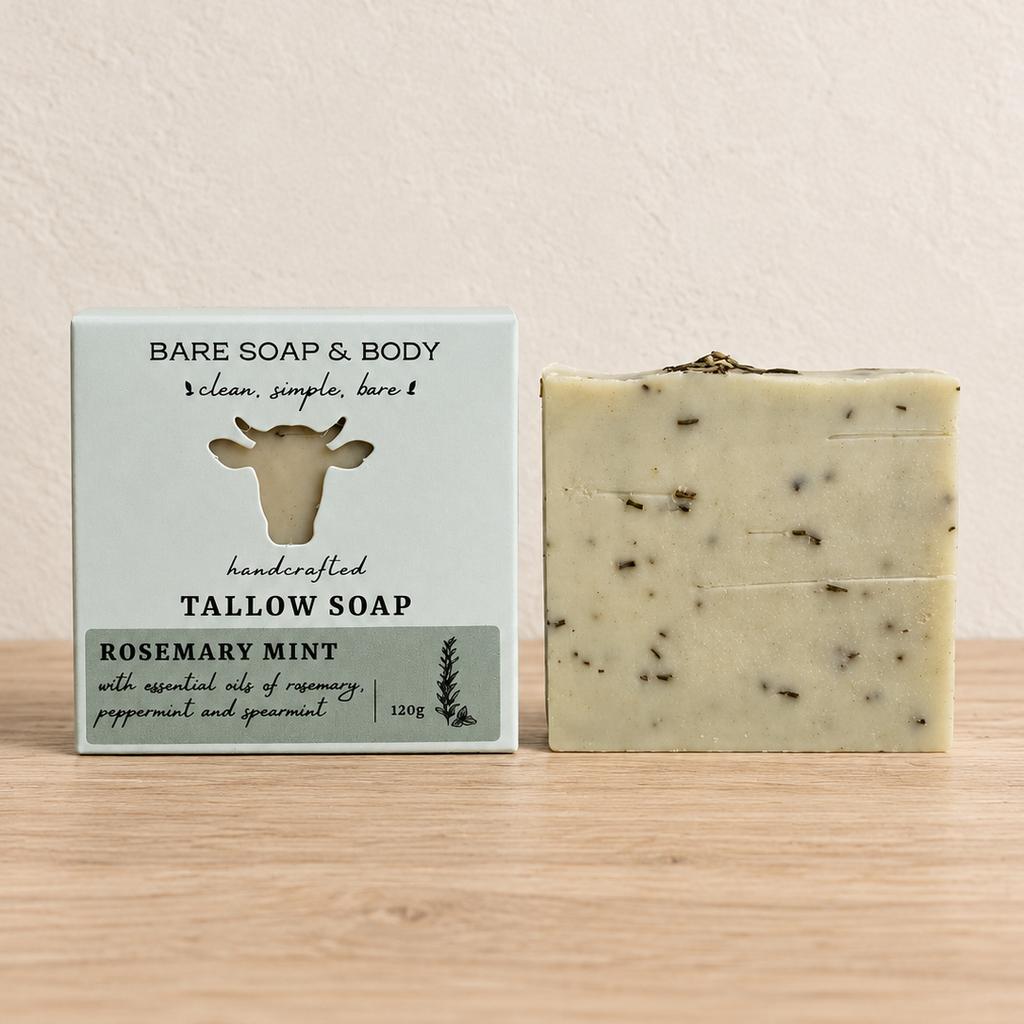 A bar of Bare Soap & Body Rosemary Mint tallow soap stands next to its light green packaging box on a light wood surface against a textured beige wall.