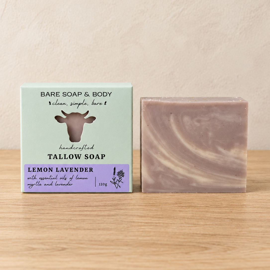 A bar of Bare Soap & Body Tallow Soap in Lemon Lavender scent, shown next to its mint green and purple cardboard packaging box on a light wooden tabletop against a textured beige wall.