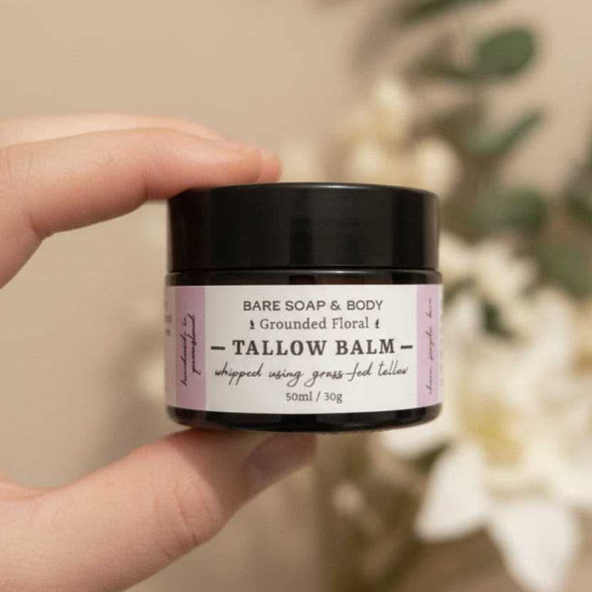 A hand holding a small black jar of Bare Soap & Body Tallow Balm against a plain light background.