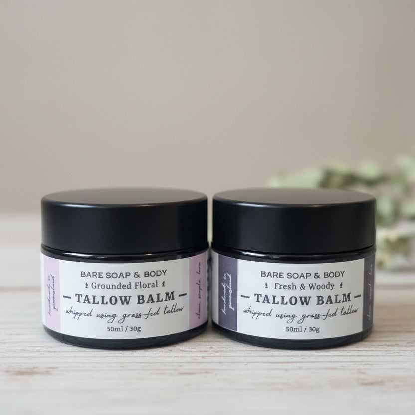Two small black jars of Bare Soap & Body Tallow Balm with white and purple labels, placed on a reflective metallic surface.