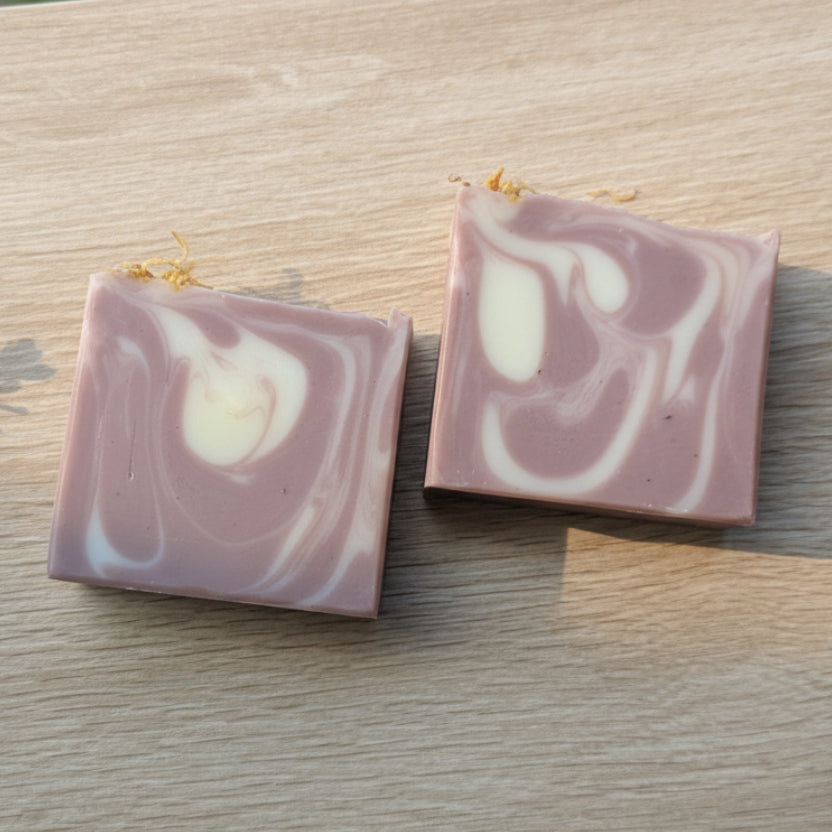 Two square purple marbled soap bars on a wooden surface.