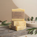 Three bars of Lemon Myrtle tallow soap stacked on a wooden surface with green leaves.