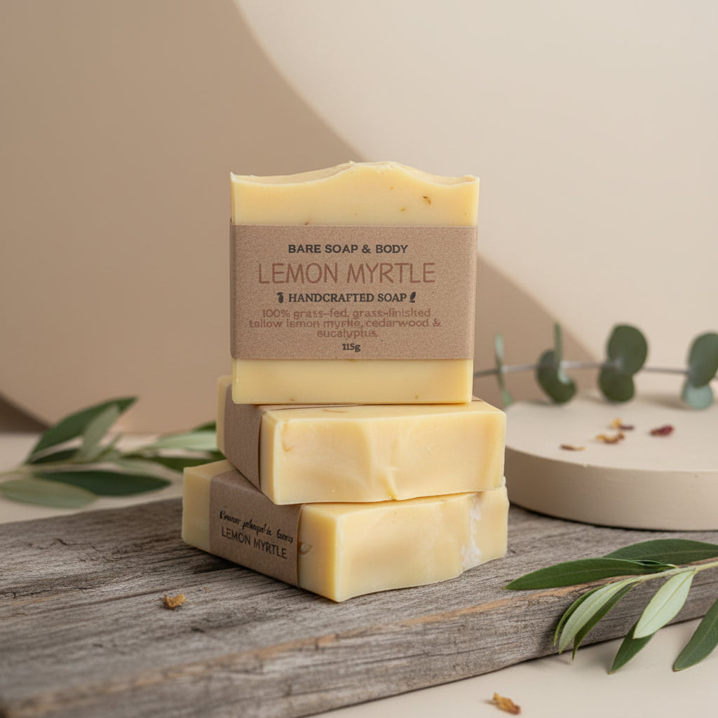 Three bars of Lemon Myrtle tallow soap stacked on a wooden surface with green leaves.