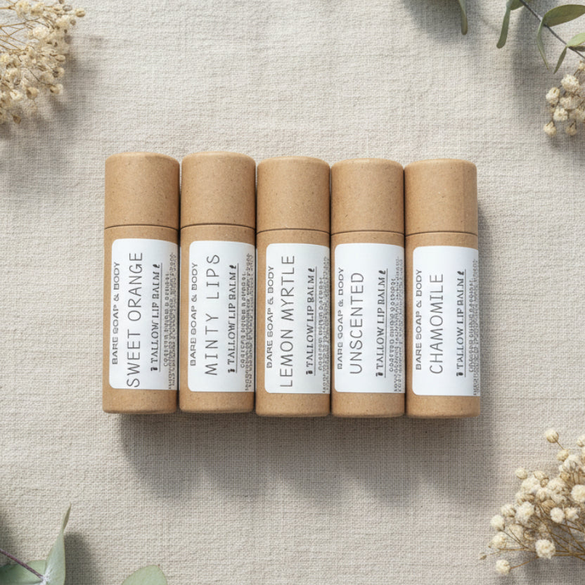Five roll-on lip balm tubes arranged side by side on a gray wood-textured surface. The tubes are light brown kraft paper with white labels reading Sweet Orange, Minty Lips, Lemon Myrtle, Unscented, and Chamomile.