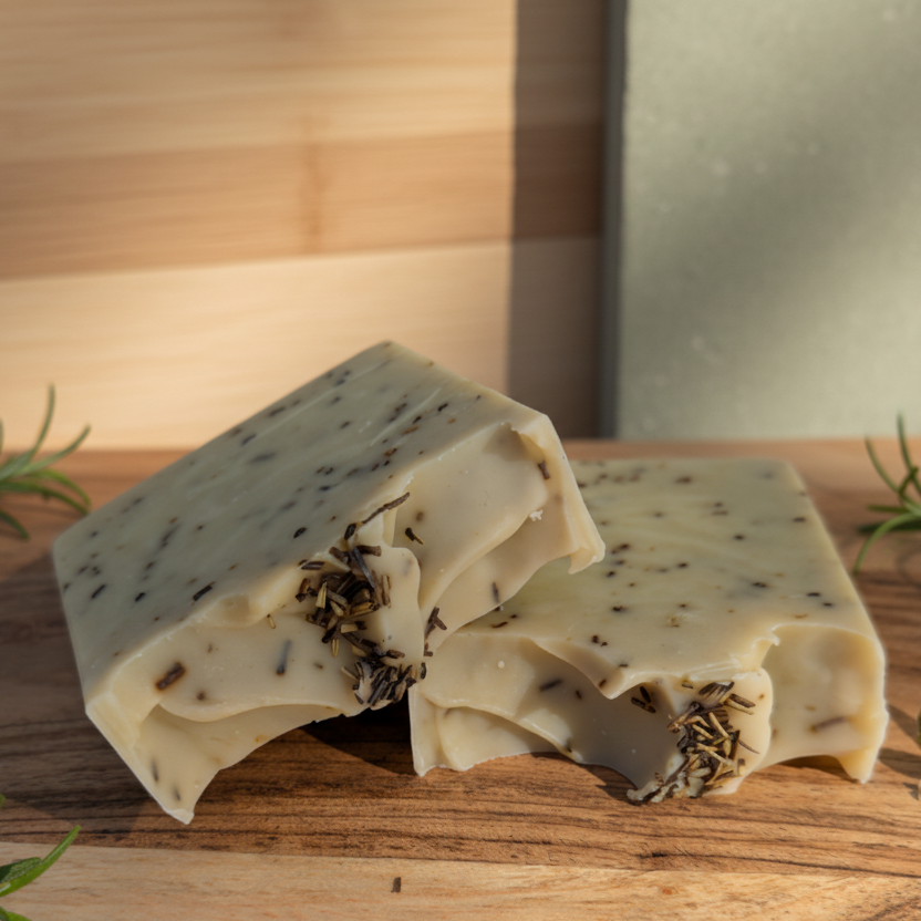 Two rosemary mint tallow soap bars with visible herbs on a wooden surface