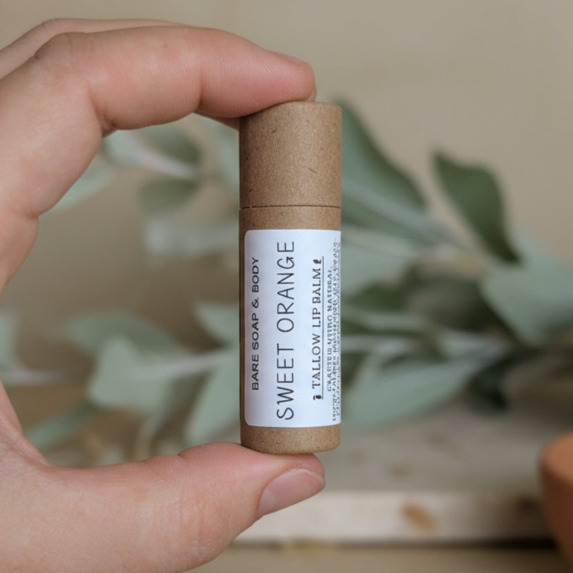 Hand holding a tallow lip balm in a kraft cardboard tube and white label.