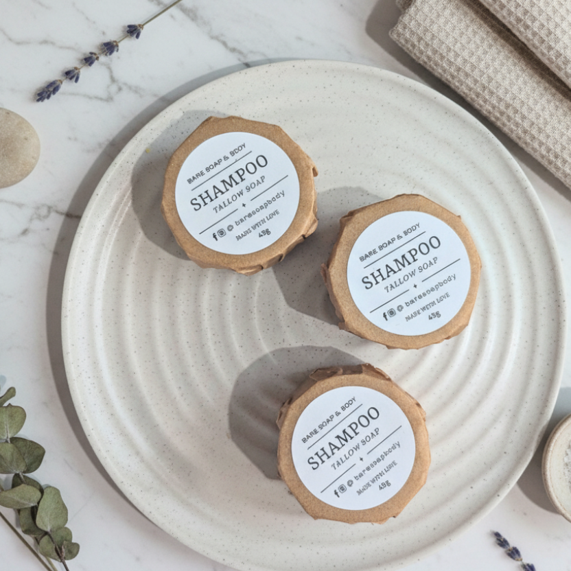 Three round containers of Bare Soap & Body shampoo soap on a textured beige surface.