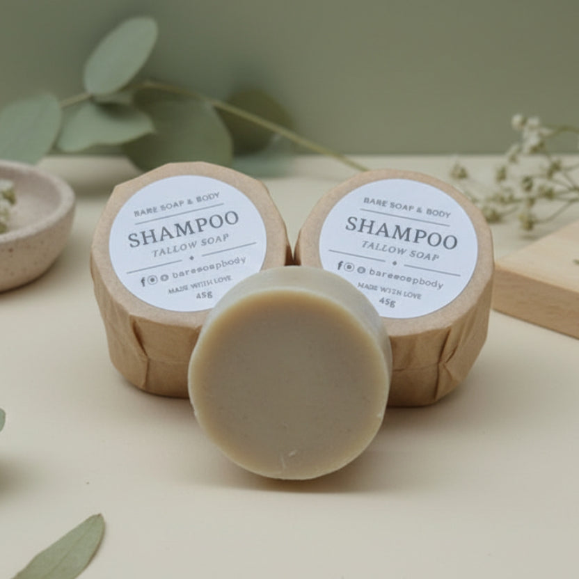 Two shampoo bars with labels on a wooden surface surrounded by green leaves.