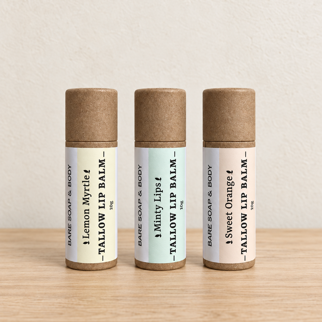 Three bare lip balm tubes standing upright on a light wood surface against a textured off-white wall. The tubes have kraft brown caps and cream labels with black text, labeled Lemon Myrtle, Minty Lips, and Sweet Orange.