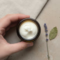 A hand holding a small round jar filled with lemon myrtle scented whipped tallow balm from Bare Soap & Body. 