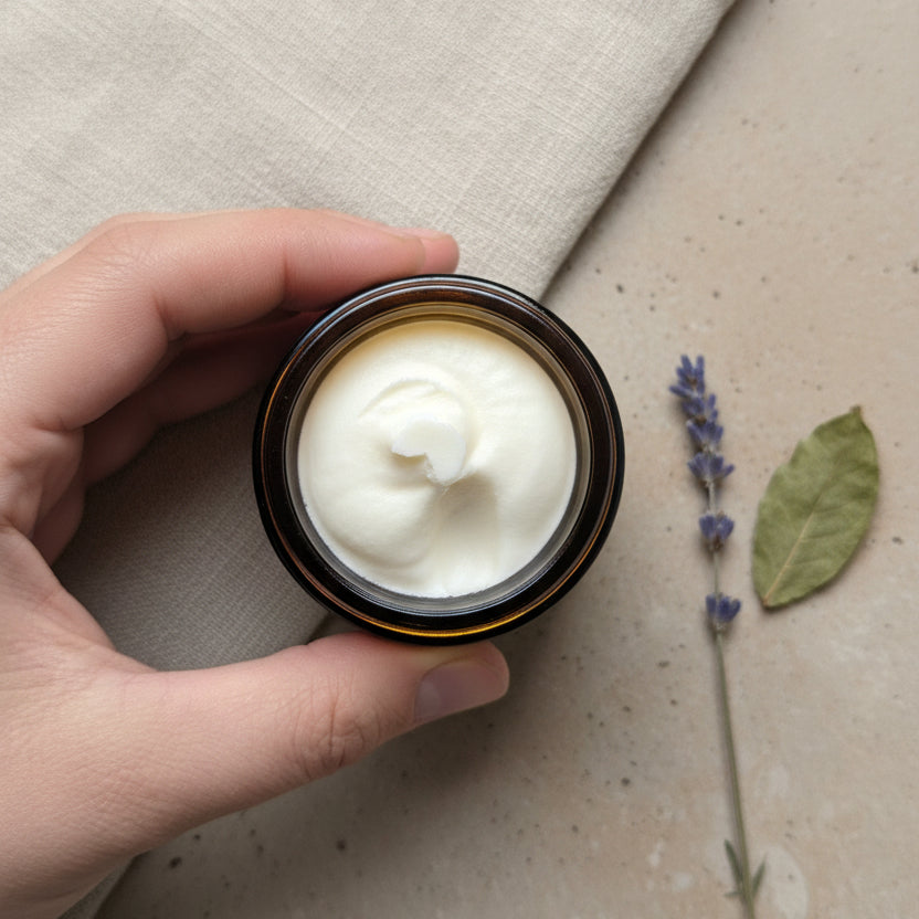 A hand holding a small round jar filled with lemon myrtle scented whipped tallow balm from Bare Soap & Body. 
