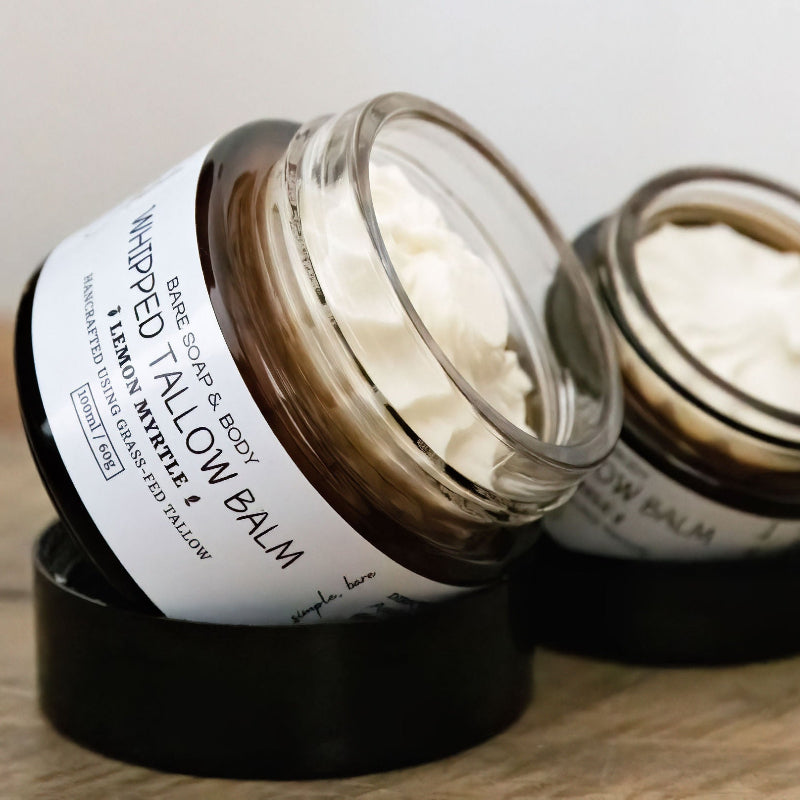 Two jars of tallow balm with visible labels on a wooden surface.