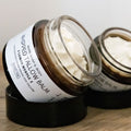 Two jars of tallow balm with visible labels on a wooden surface.