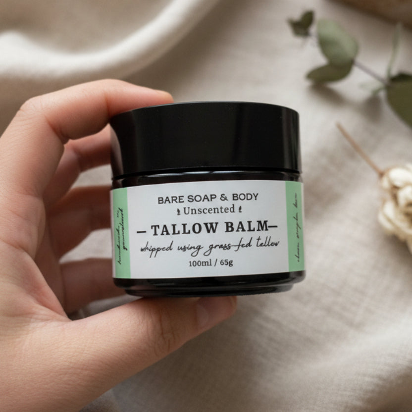 A hand holding a small black jar of Bare Soap & Body Tallow Balm against a dark woven background.