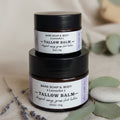 Two small jars of Bare Soap & Body Tallow Balm in lavender scent, stacked on a dark woven wicker surface.