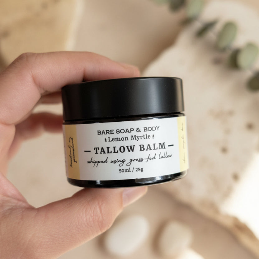 A hand holding a small black jar of Bare Soap & Body Tallow Balm with a cream-colored label, set against a woven brown background.