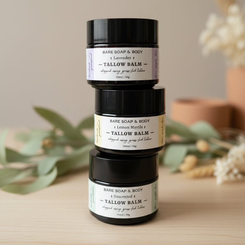 Three containers of tallow balm stacked on a wooden surface with a blurred background.